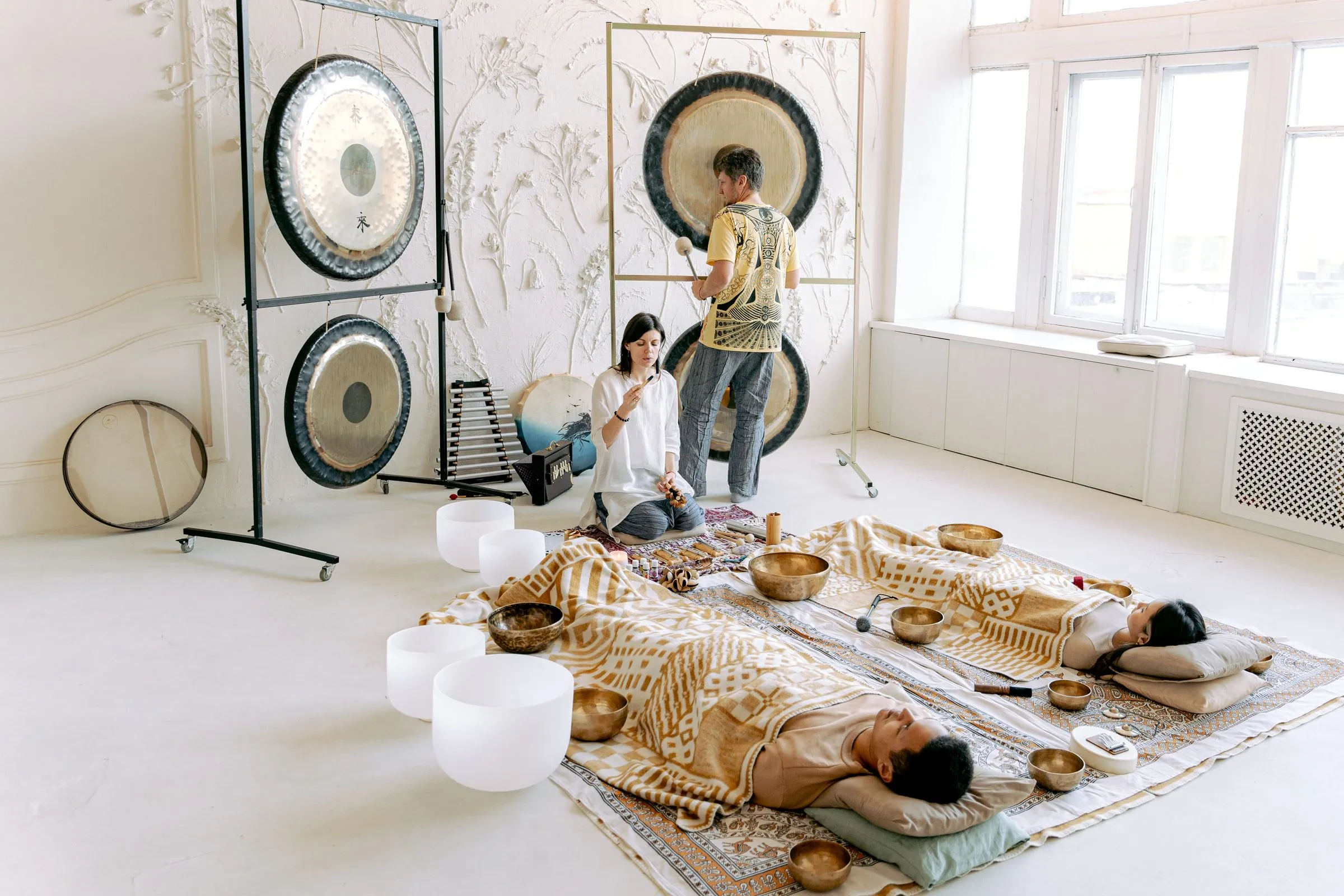 A group lying in a circle around singing bowls during a sound bath